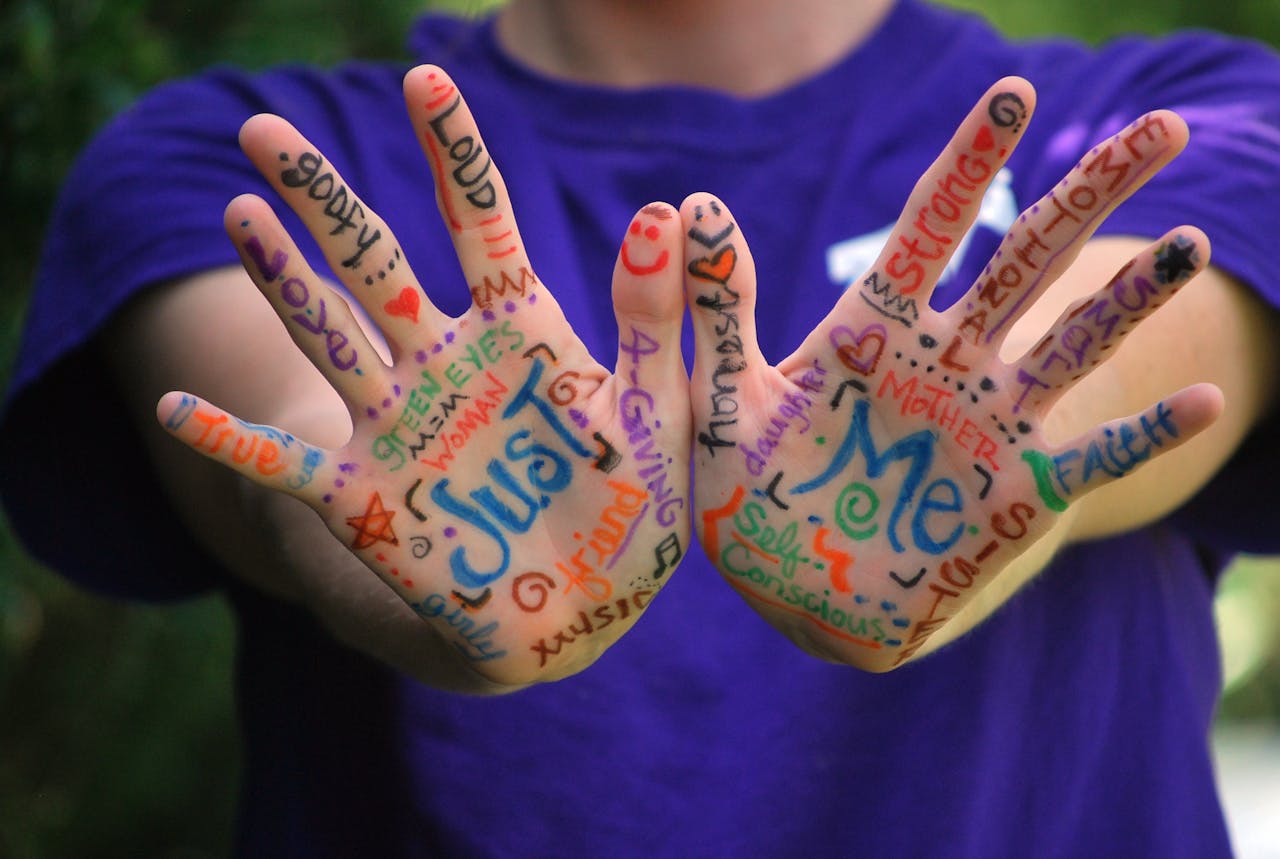 Colorful words and symbols drawn on open hands expressing emotions and identity.