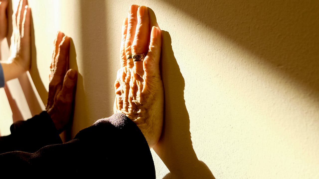 Hands of different ages touching a sunlit wall, symbolizing connection across generations.